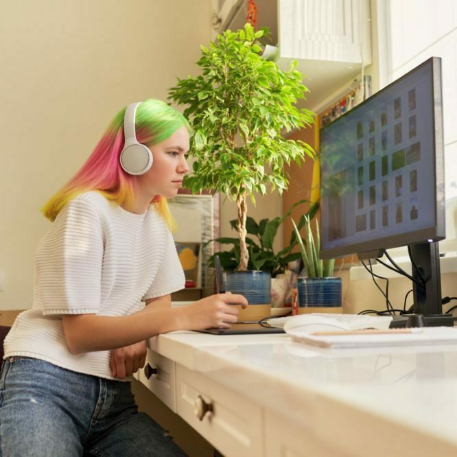 Girl teenager artist in headphones drawing on computer using graphics tablet